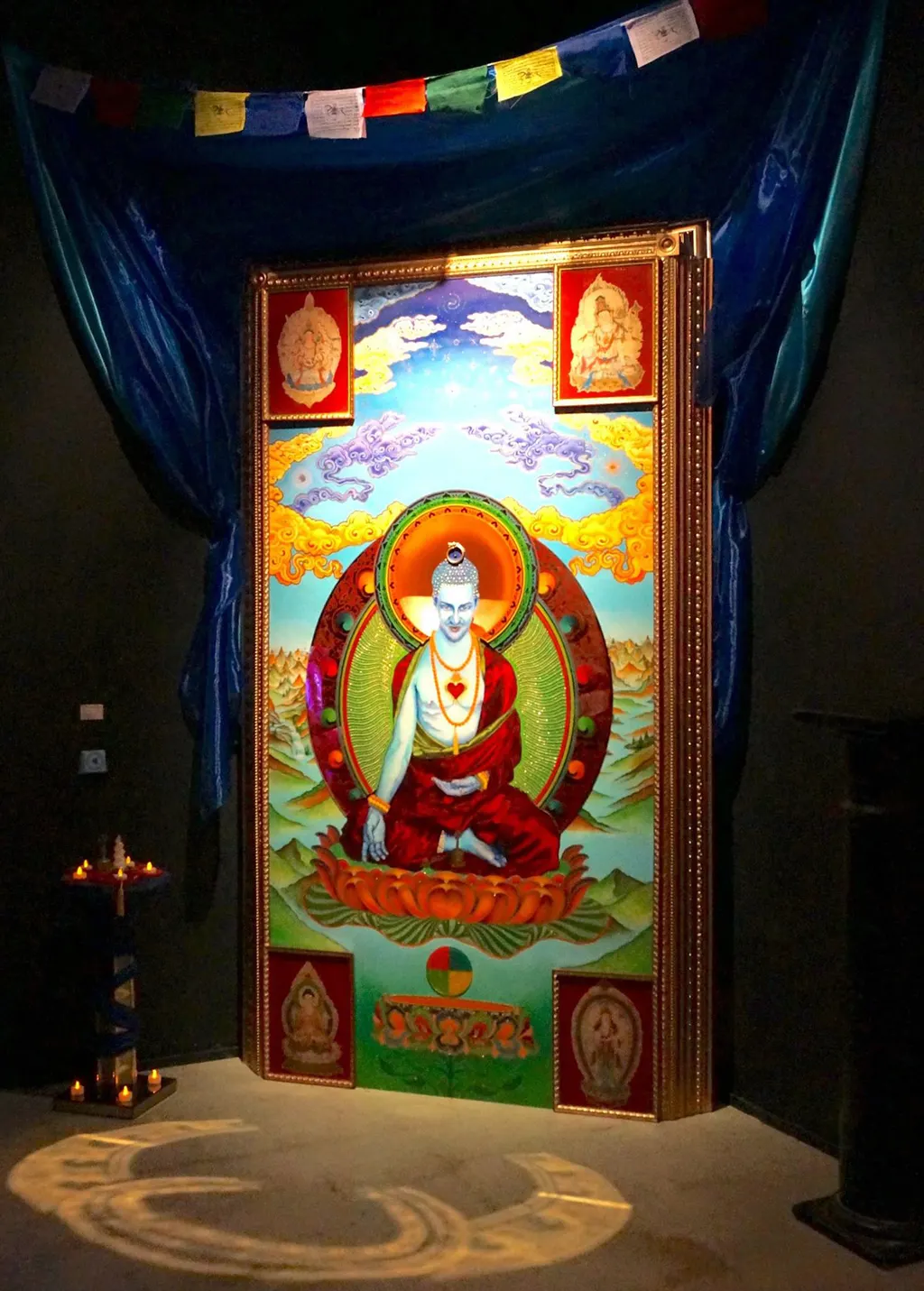The installation: the painting in a gilded shrine, lit, beneath prayer flags